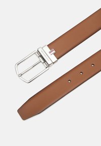 Cintura in pelle marrone con fibbia rettangolare color argento. La fibbia presenta un piccolo accento a righe. Estremità piatta con fori per la regolazione.