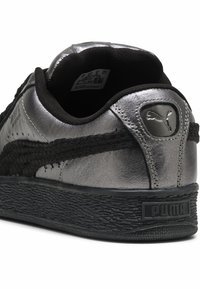Schwarzer und metallisch silberner Sneaker mit einer strukturierten Gummisohle, PUMA-Logo an der Ferse und einem glatten Obermaterial mit schwarzen Akzenten.