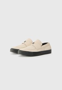 Beige slip-on sko laget av glatt semsket skinn, svart gummisåle og stjernedetaljer på oversiden. Enkelt design med lav profil.