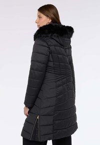 Černý prošívaný kabát s kapucí, s kožešinovým lemem na límci, prošívaným vzorem a zkosenými zipy na bocích pro větší detail.