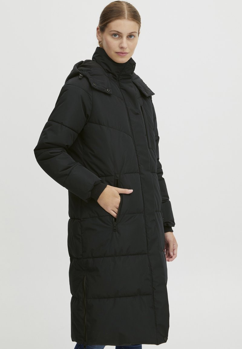 Cappotto lungo nero imbottito con colletto alto, tasche con cerniera e design trapuntato con una texture liscia e silhouette aderente.