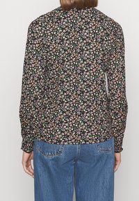 Bloem blouse met een zwarte achtergrond, met kleine roze, gele en groene bloemen. Lange mouwen en een gegatherde zoomdetail.