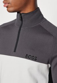 Mörkgrå och vit halvdragspullover i mjuk stickad tyg, med svart broderad "BOSS"-logotyp samt ribbad krage och ärmar.