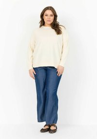 Cremefarbiges, oversized Sweatshirt mit langen Ärmeln, kombiniert mit weit geschnittenen blauen Jeans. Die Schuhe bestehen aus flachen Schuhen mit schwarzem und braunem Leopardenmuster.