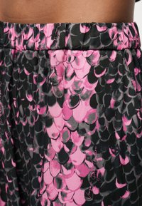 Κοντινή λήψη της μέσης που φοράει μαύρη και ροζ φούστα ή παντελόνι με ελαστική ζώνη και αφηρημένο σχέδιο που μοιάζει με λέπια.