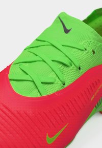 Εγγύς λήψη αθλητικού παπουτσιού Nike σε νέον πράσινο και κόκκινο, με υφή στην επάνω επιφάνεια, κορδόνια και μικρό πράσινο λογότυπο Nike στην κόκκινη περιοχή.