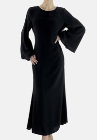 Schwarzes langärmliges Kleid mit tailliertem Oberteil und ausgestelltem Rock. Glatter Stoff, runder Ausschnitt und weite, schwingende Ärmel verleihen Struktur. Keine Muster oder Verzierungen.