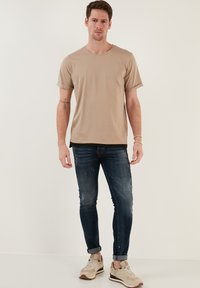 Beige T-Shirt mit kurzen Ärmeln, kombiniert mit dunkelblauen, verwaschenen Jeans. Getragen mit beigen und grauen Turnschuhen. Schlichte, legere Kleidung.
