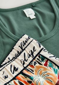 Grünes, geripptes Tanktop mit einem farbenfrohen Rock mit abstrakten Formen und schwarzem Schriftzug auf einem cremefarbenen Bund.