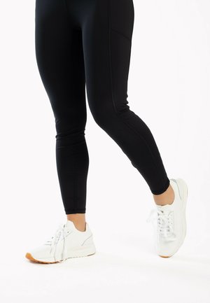 Schwarz legging mit einem taillierten Design und kontrastierenden Nähten, kombiniert mit weißen Sportschuhen mit strukturiertem Obermaterial und orangefarbener Sohle.