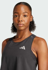 Sort atletisk tanktop med en tekstureret overflade, der har et kontrastgry logo på brystet og en ærmeløs design.