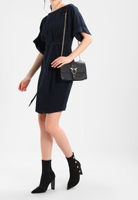 Granatowa sukienka na krótki rękaw z pasem w talii. Czarna torebka na łańcuszku z okrągłym zapięciem. Czarne botki za kostkę z złotymi detalami w postaci guzików.