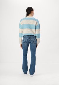 Striped sweater in light blue and beige wool blend, paired with fitted dark blue flared jeans. Model shows back view, with white sneakers.