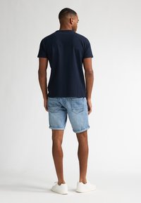Camisa azul marino de manga corta con textura, combinada con pantalones cortos de mezclilla azul claro enrollados y zapatillas blancas. Diseño sencillo y casual.