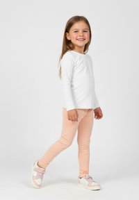 Biała bluzka z długim rękawem, jasnoróżowe legginsy i białe trampki z pastelowymi akcentami. Strój jest prosty i dopasowany, podkreślając komfort.