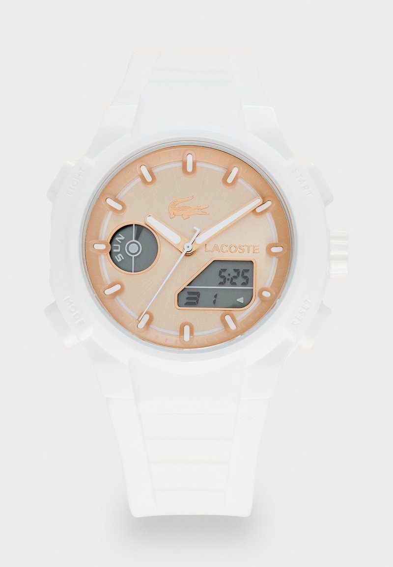 Montre Lacoste avec un bracelet en silicone blanc, un cadran beige rond, des accents dorés, affichage analogique et numérique, et un détail de logo à 12 heures.