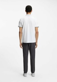 Camiseta tipo polo blanca, de manga corta con ribete negro; combinada con pantalones gris oscuro, de corte ajustado y textura suave. Zapatillas blancas completan el conjunto.
