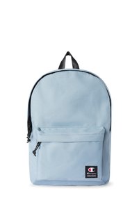 Mochila azul claro hecha de tela duradera, con un bolsillo frontal con cremallera, cremallera negra y un asa en la parte superior. Parche de logotipo icónico en la parte frontal.