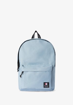 Mochila azul claro hecha de tela duradera, con un bolsillo frontal con cremallera, cremallera negra y un asa en la parte superior. Parche de logotipo icónico en la parte frontal.