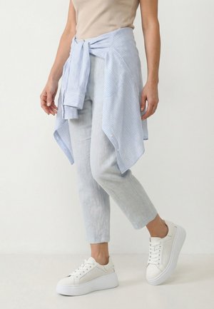 Kvinde iført lyseblå korte bukser, hvide platform-sneakers og en lyseblå stribet skjorte bundet omkring taljen.