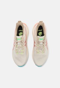 Light beige running shoes with a textured upper, pink and green accents, and lace-up design. Features a cushioned sole and logo detail.