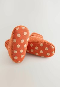 Chaussons orange en peluche avec des semelles texturées, ornés d'un motif de citrouille. Matériau doux et bords côtelés pour plus de confort.