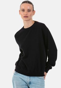 Pull en maille noir avec un col rond et des manches longues, doté d'une coupe décontractée. Associé à un jean en denim bleu clair.