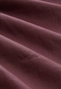 Tissu tissé en mauve profond, présentant une surface texturée avec des plis verticaux prononcés et une finition lisse, créant une apparence structurée.