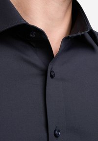 Zwarte button-up blouse met een gestructureerde kraag, een gladde textuur en donkere knopen, die een op maat gemaakte uitstraling heeft.