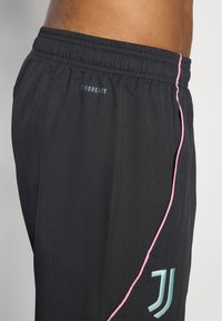 Svarte atletiske shorts med elastisk midje, med en rosa stripe på siden og "AEROREADY"-merket sydd på baksiden.