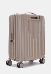 Hard-shell suitcase in beige, featuring vertical ridges, a top handle, combination lock, and four black wheels for mobility.