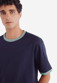 Mörkblå bomullströja med korta ärmar, som har en ljusgrön ribbad halsringning och ärmslut. Slät konsistens, minimal design.