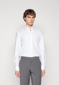 Camicetta bianca a maniche lunghe con colletto a punta, abbinata a pantaloni grigi con texture, caratterizzati da una vestibilità slim e tessuto morbido.