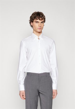 Camicetta bianca a maniche lunghe con colletto a punta, abbinata a pantaloni grigi con texture, caratterizzati da una vestibilità slim e tessuto morbido.