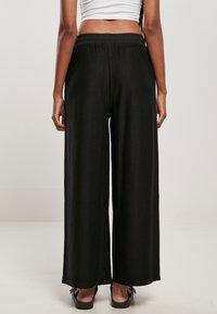 Pantalons larges noirs en tissu texturé et côtelé. Dotés d'une taille élastique, ils tombent jusqu'aux chevilles et se portent avec des chaussures plates.