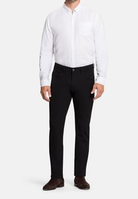 Bílá košile s knoflíky a náprsní kapsou, spárovaná s černými slim-fit kalhotami a tmavě hnědou obuví. Hladká textura látky.