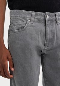 Des jeans en denim gris présentent un design classique à cinq poches, des coutures discrètes et un petit logo sur la poche arrière. Matériau durable de haute qualité.