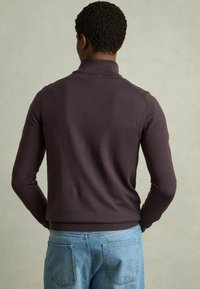 Pulover tricotat de culoare mov închis, cu guler înalt, siluetă ajustată și manșete din tricot, asortat cu blugi din denim de culoare albastră deschisă.