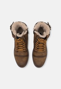 Stivali alla caviglia in finta pelle marrone con fodera in pelliccia beige, lacci dorati e suola robusta; presenta una fibbia sul lato per la regolazione.