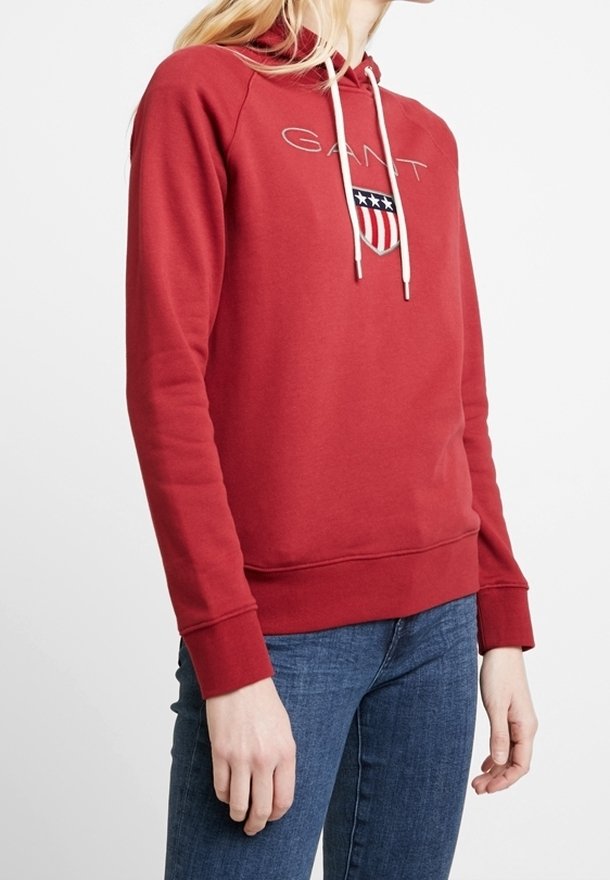 Sudadera con capucha roja con cordones blancos, presenta un logo y un diseño de escudo con estrellas. Tejido suave, puños y cintura acanalados.