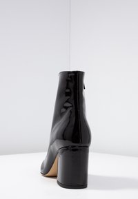 Black patent leather ankle boots with a high block heel, smooth surface, and a simple design, featuring a zipper closure on the back.