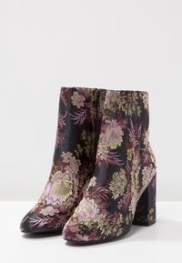 Bottes noires à la cheville avec un motif floral rose et vert, dot ées d'un bout pointu et d'un talon épais. Texture satinée.