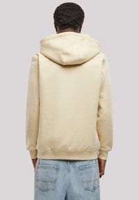 Cream-colored hooded sweatshirt with a soft texture, featuring a relaxed fit and side pockets, paired with light blue jeans.