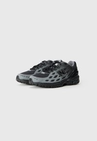 Baskets de sport noires et grises avec tige en mesh, bout arrondi et semelle en caoutchouc texturé. Comprend un système de laçage et un logo sur le côté.