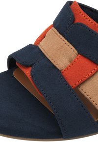 Gros plan sur une sandale en suède marine, orange et beige, avec une large sangle et un design à bout ouvert.