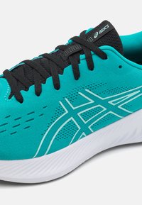 Chaussure de course turquoise avec un dessus en mesh respirant, des lacets noirs et une semelle blanche. Présente un design graphique marquant et des accents texturés.