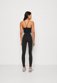 Top desportivo preto com alças finas, combinado com leggings pretas de cintura alta com riscas brancas nas laterais. Modelo vista de costas.