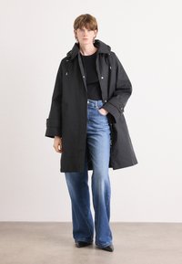 Black waterproof coat with a hood, featuring zippered front, side pockets, and adjustable cuffs, paired with flared denim jeans.