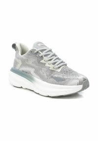 Zapato atlético gris hecho de malla transpirable con un patrón texturizado. Presenta una suela blanca gruesa y acentos en gris claro en los costados y en los cordones.