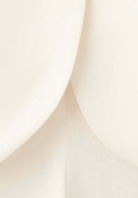 Gros plan d’un tissu doux de couleur crème avec des plis courbes qui se chevauchent, créant une texture lisse et stratifiée.